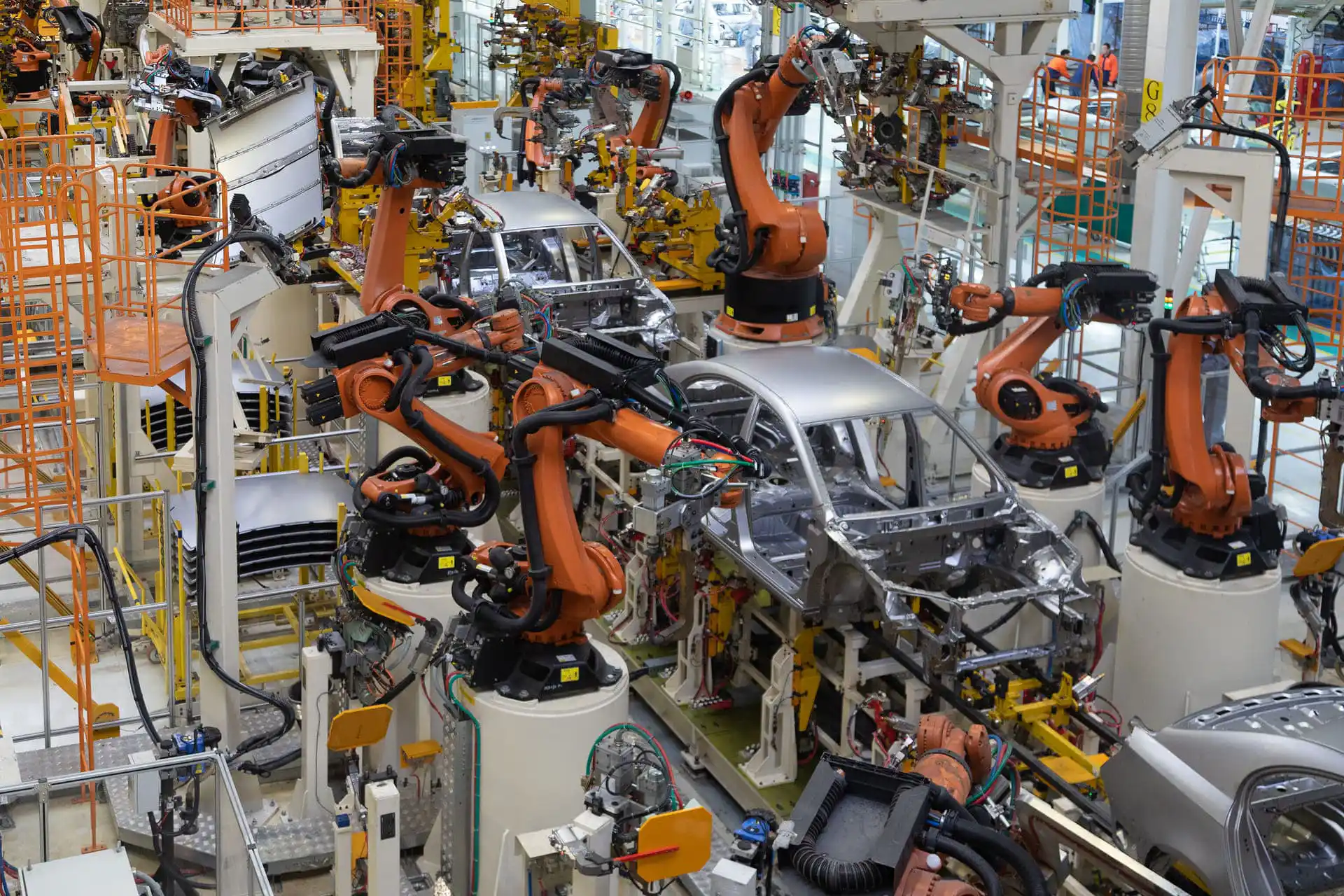 Automatisierte Fahrzeugmontage in einer modernen Autofabrik: Mehrere orangefarbene Industrieroboter arbeiten synchron an Fahrzeugkarosserien in einer hochentwickelten Produktionslinie.