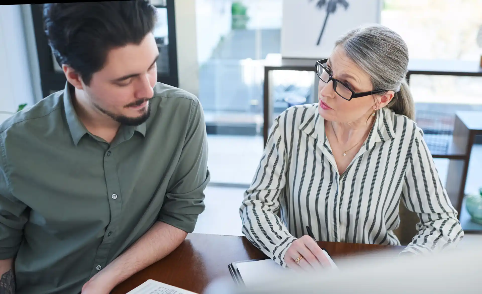 Ältere Frau und jüngerer Kollege besprechen gemeinsam Unterlagen im modernen Büro – steht für generationenübergreifende Zusammenarbeit und Planung unter Berücksichtigung des Arbeitszeitgesetzes.